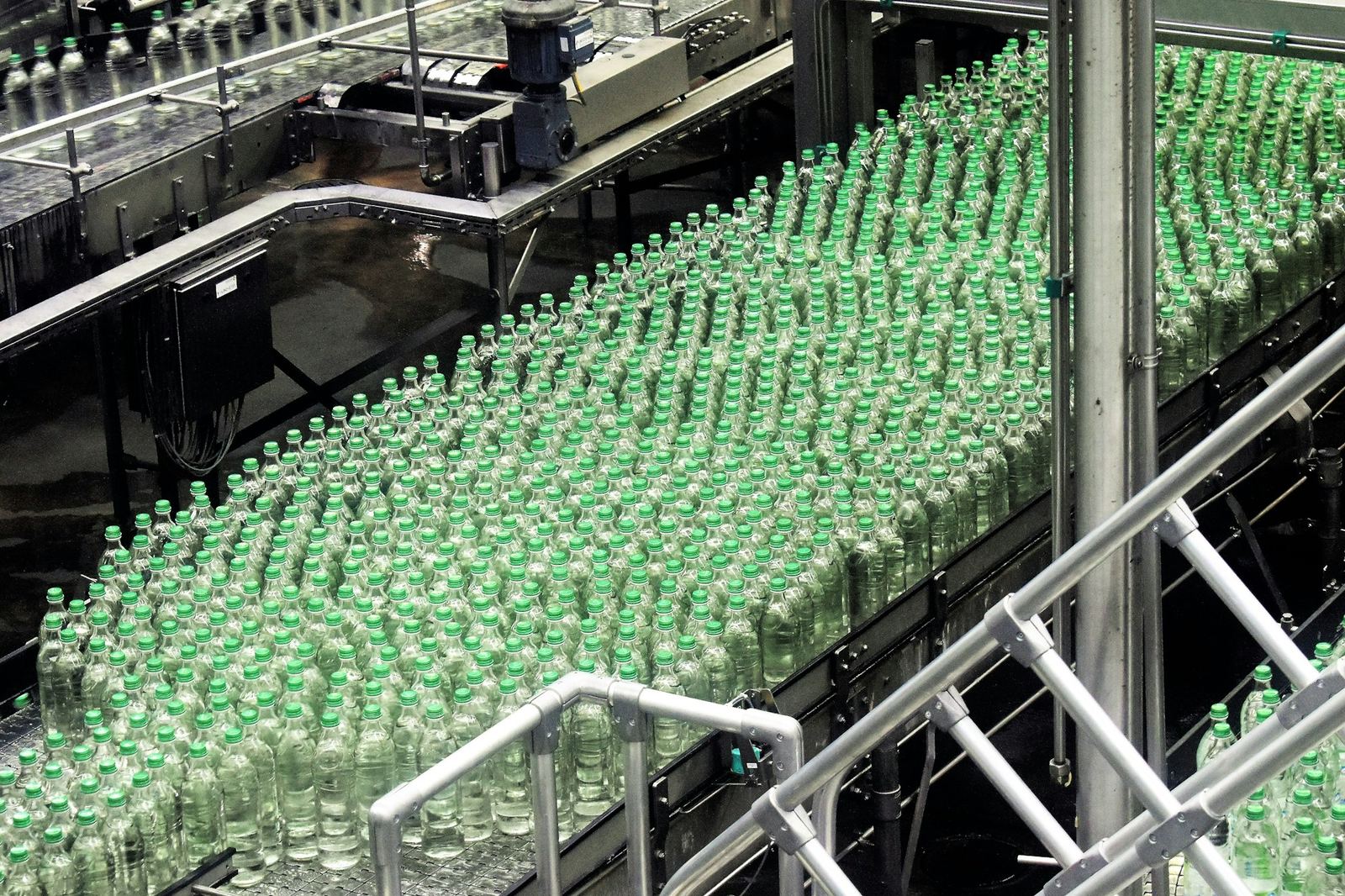 Hundreds of green-capped glass bottles move along conveyors on a bottling line.
